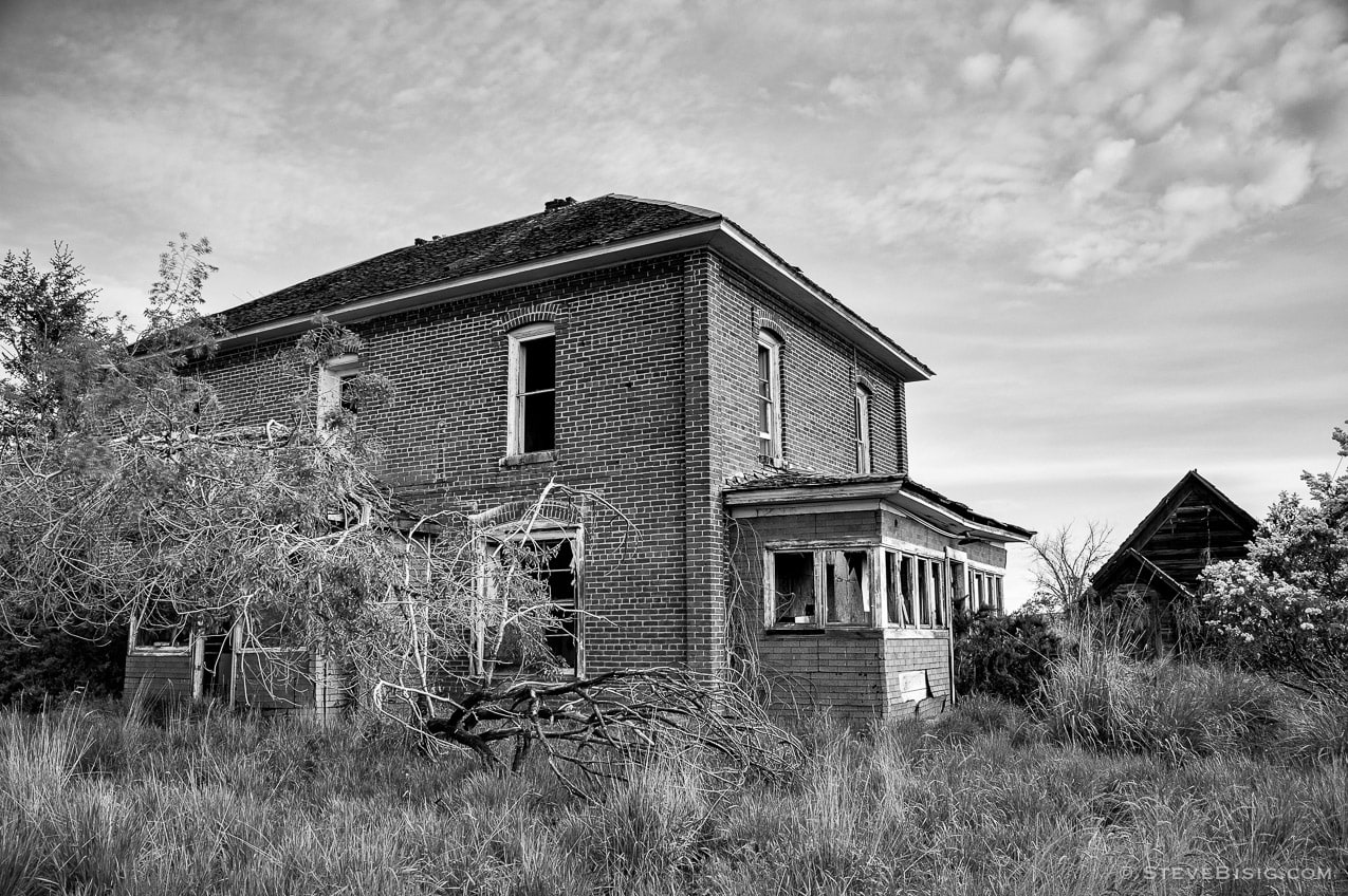 A black and white photograph of an abandoned brick farm house on D Road NW in rural Douglas County, Washington