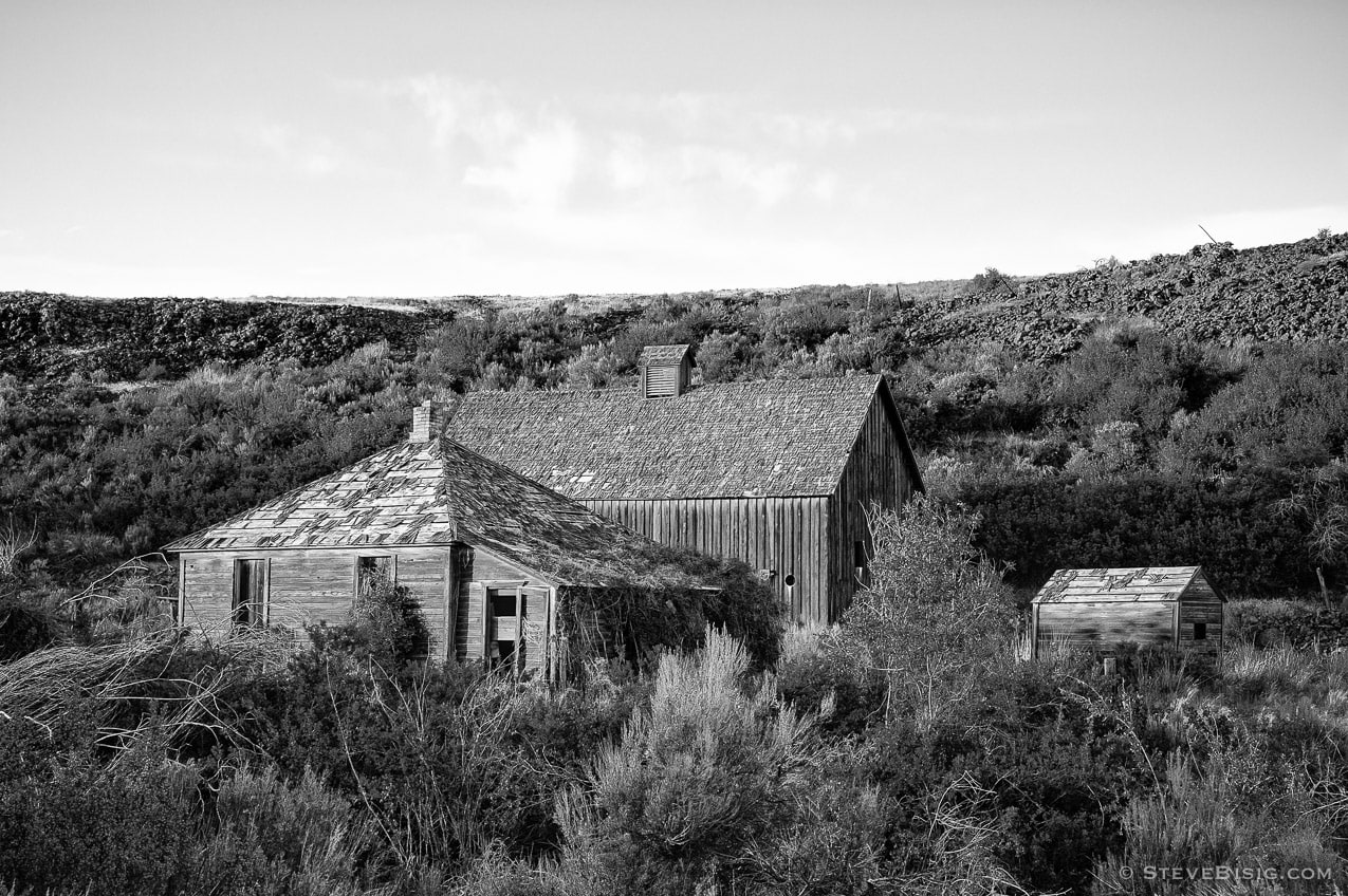 A black and white photograph of an old abandoned house and barn in rural Alstown, Washington.