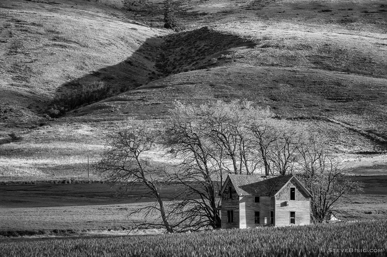 A black and white photograph of an abandoned two-story farmhouse on P Road NW in rural Douglas County near Waterville, Washington.
