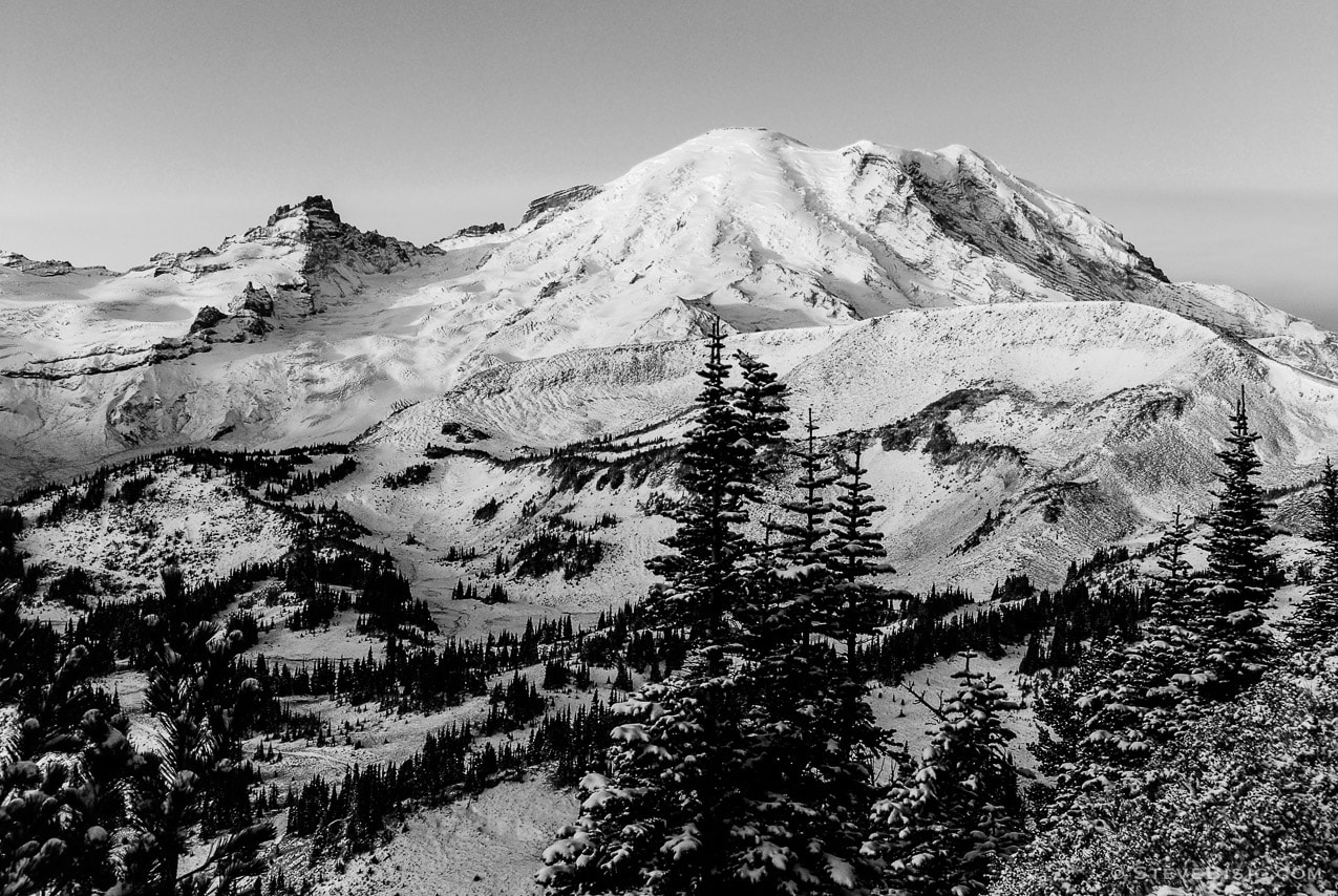 A black and white photograph of the autumn sunrise shining on Mount Rainier and Little Tahoma after the first snowfall of the season. Viewed from the Sunrise area of Mount. Rainier National Park, Washington
