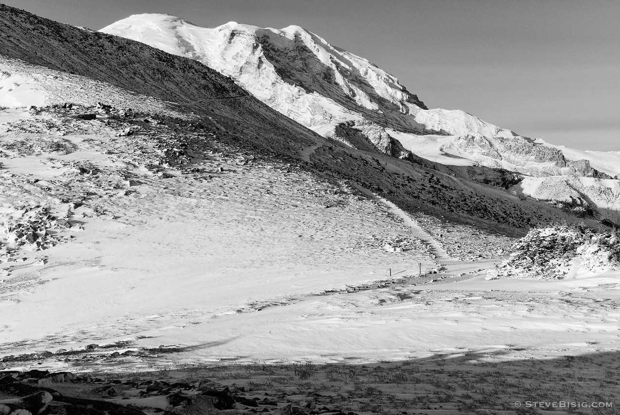 A black and white photograph of the Burroughs Mountain Trail after an early Autumn snow with Mount Rainier in the background.