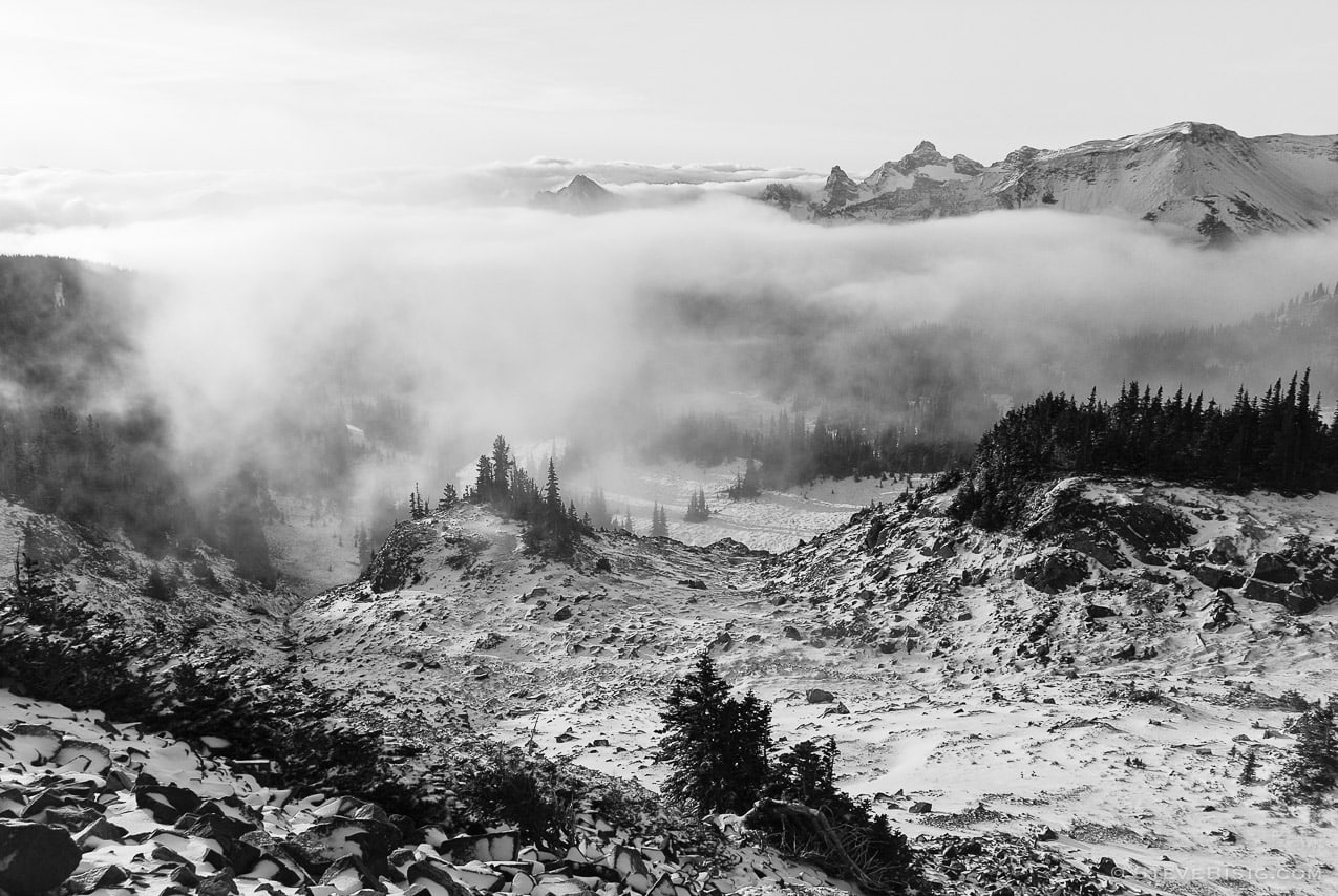 A black and white photograph of clouds rolling into a valley near the Sunrise area at Mount Rainier National Park, Washington.