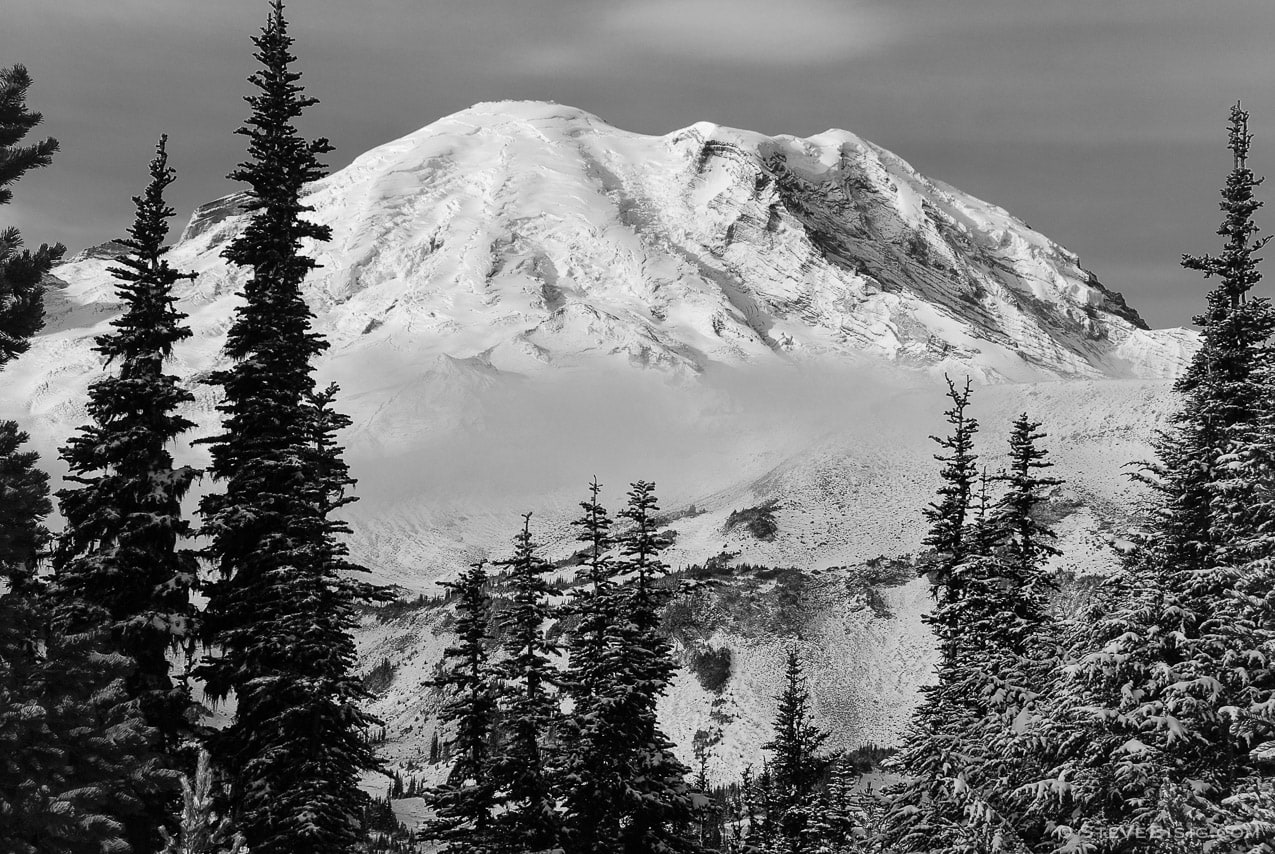 A black and white photograph of Mount Rainier framed in by an opening in the alpine forest near Sunrise at Mount. Rainier National Park, Washington.