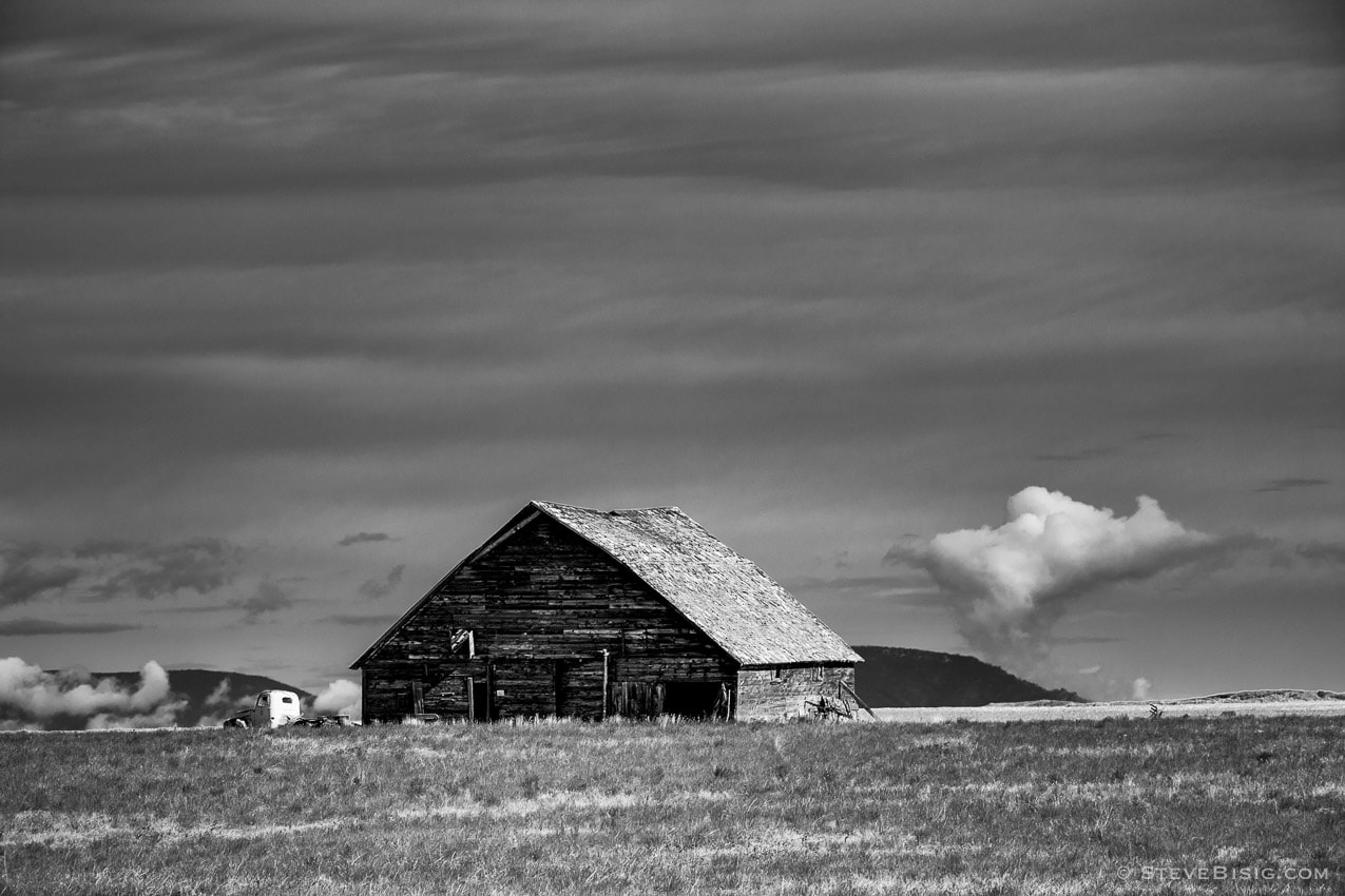 A black and white photograph of an old barn and truck on a farm in rural Douglas County, Washington.
