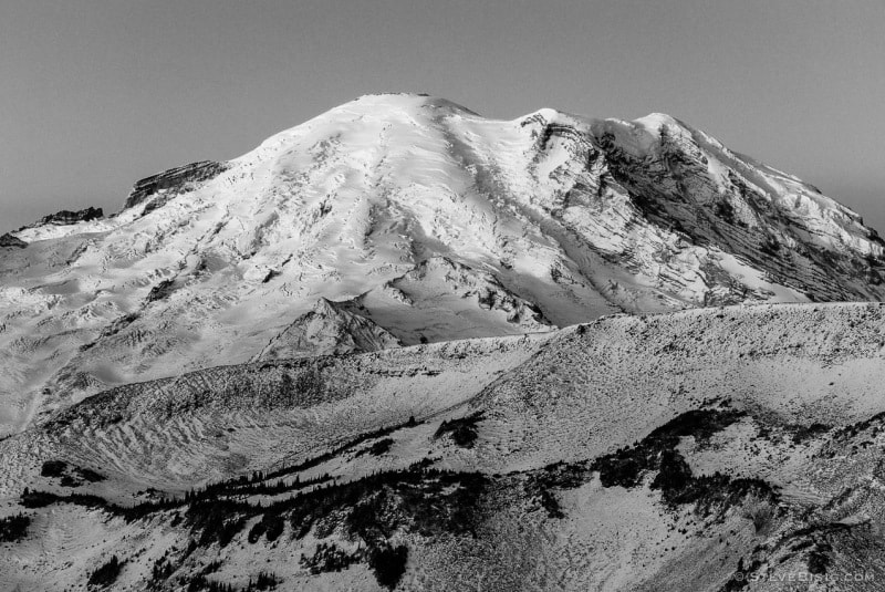 A black and white photograph of the rising sun shining on Mt. Rainier as viewed from Sunrise, Mt, Rainier National Park, Washington.