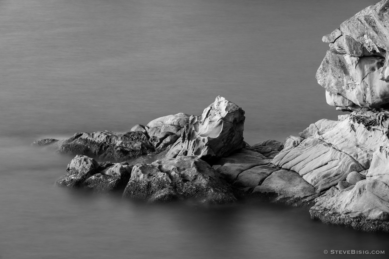 A long exposure fine art black and white photograph of sandstone formations at high tide along the coastline at Larrabee State Park in Whatcom County near Bellingham, Washington.