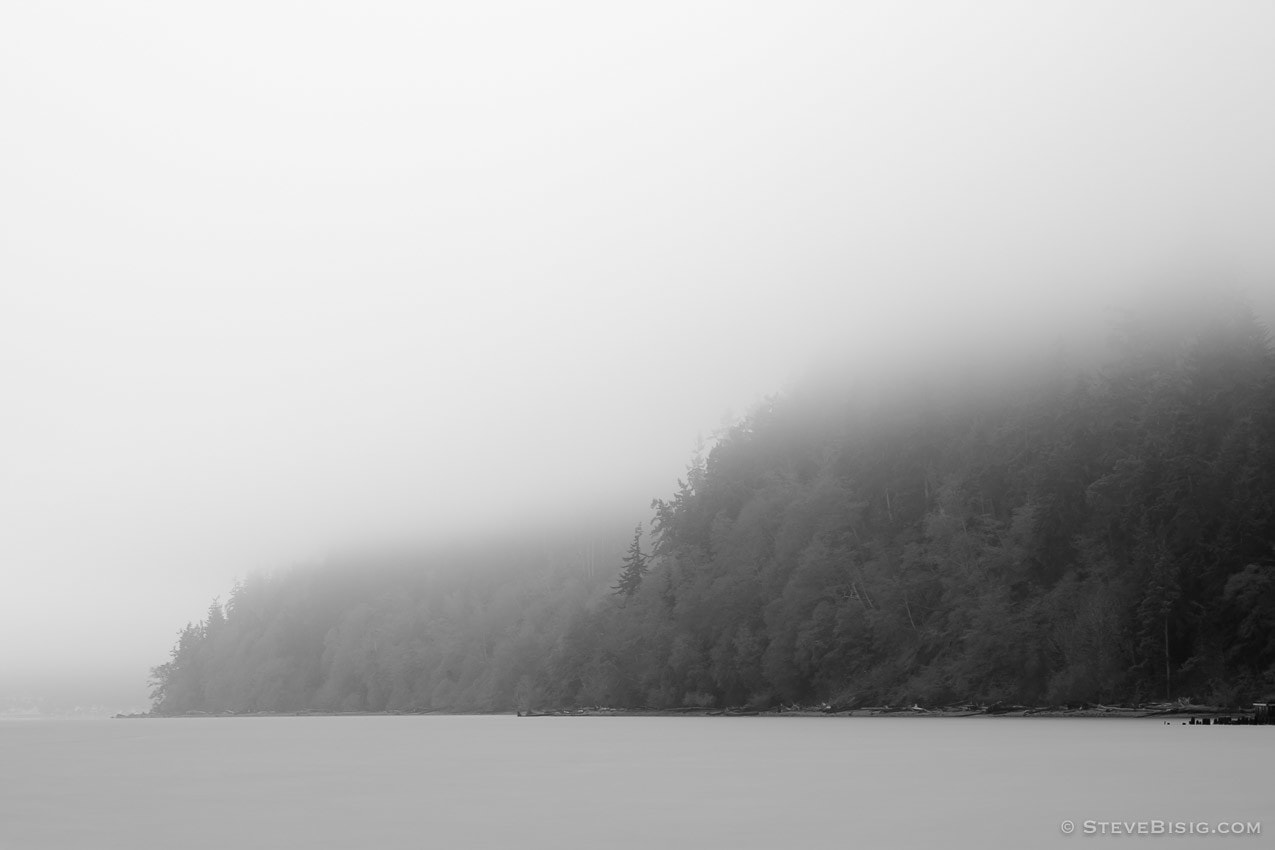 A fine art black and white long exposure photograph of the misty shoreline near Ala Spit on Whidbey Island, Washington.