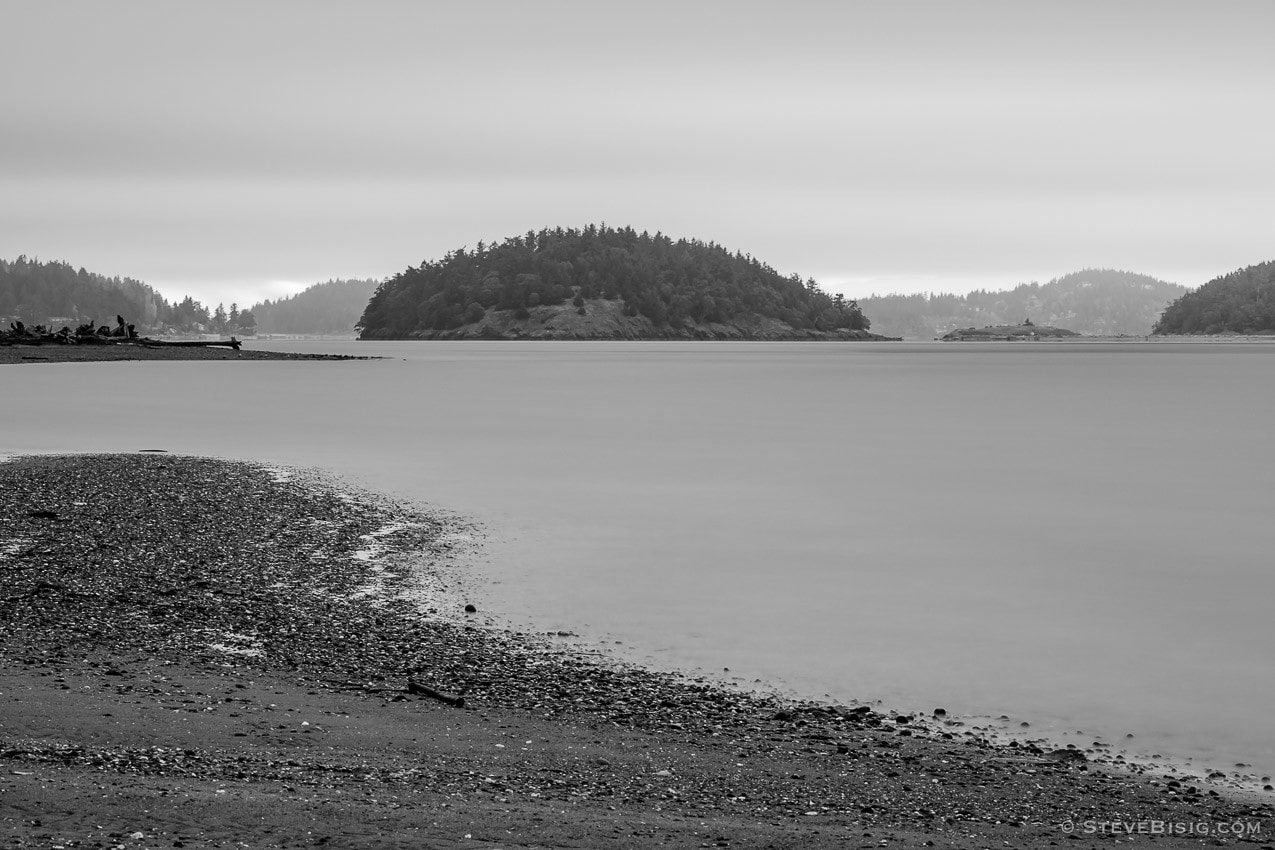 A black and white long exposure photograph of Skagit Island on a cloudy day as viewed from Ala Spit on Whidbey Island, Washington.