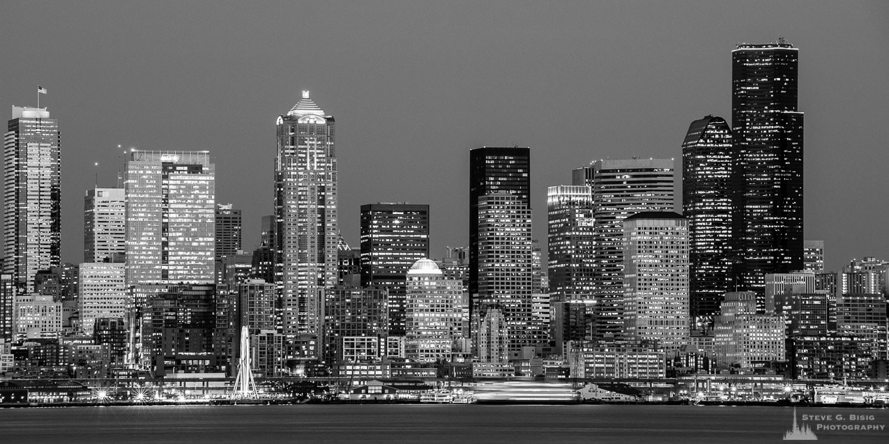A black and white panoramic photograph of downtown Seattle, Washington skyline over Elliott Bay on a late Winter night.