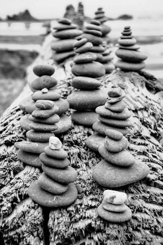 A black and white photograph of rock cairns on a log at Ruby Beach in the Olympic National Park in Washington State.