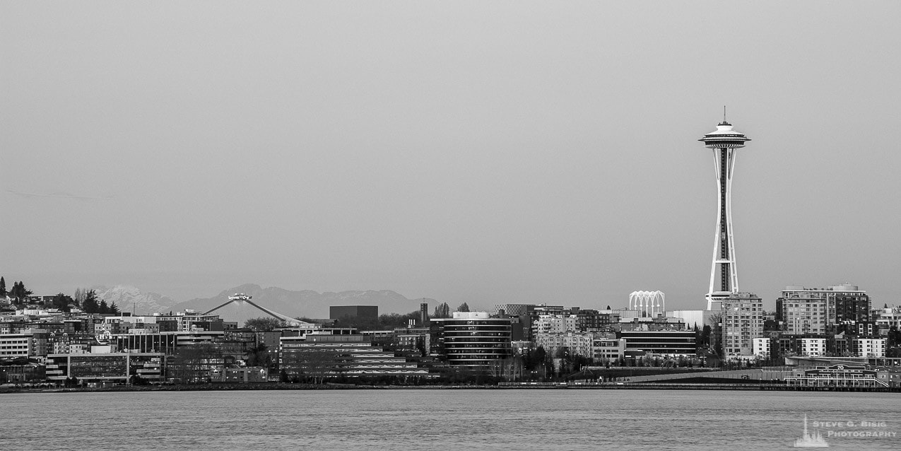 A black and white panoramic photograph of the Space Needle and the Seattle, Washington skyline over Elliott Bay as seen from Alki Point just before dusk on a late Winter evening.
