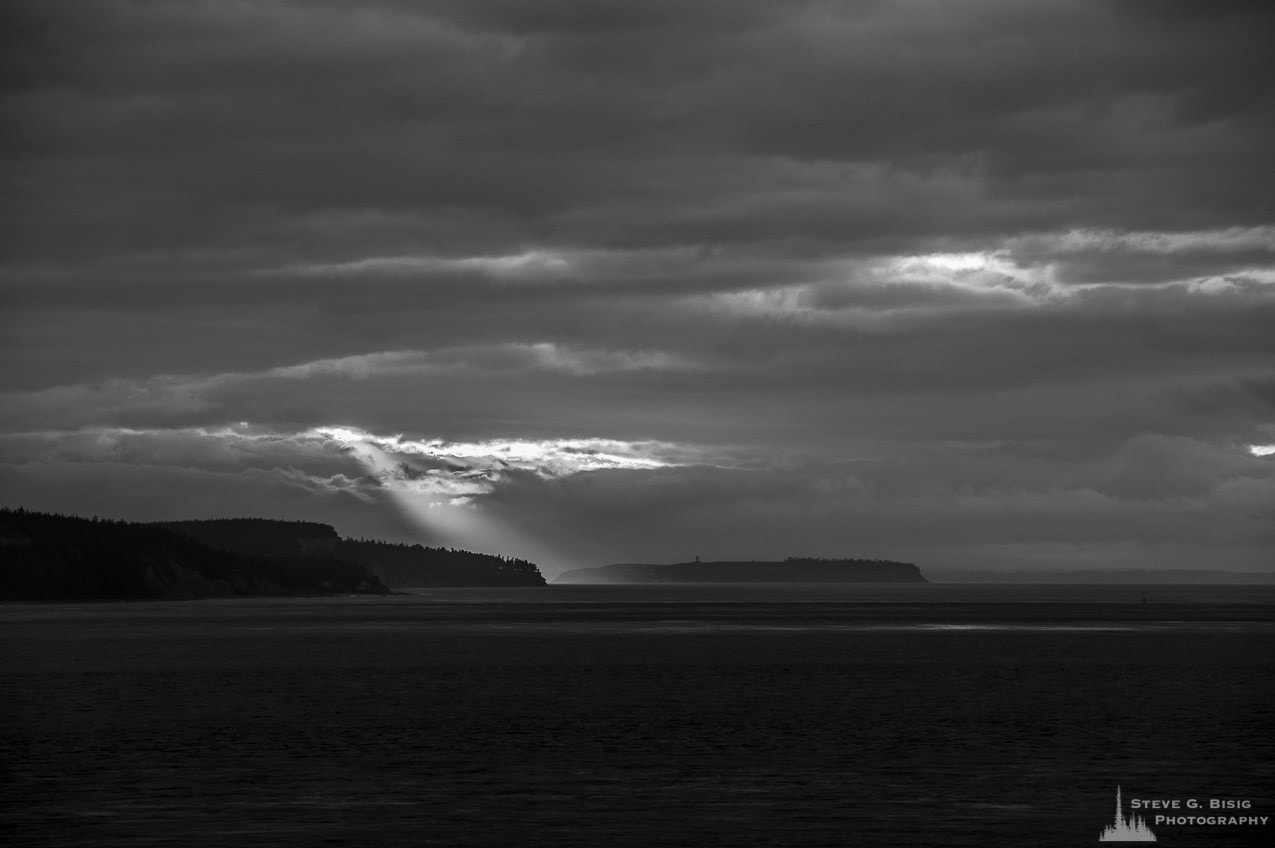 A black and white photograph of sunrays peaking through the clouds over the Puget Sound on a dark Winter day as viewed from Whidbey Island, Washington.