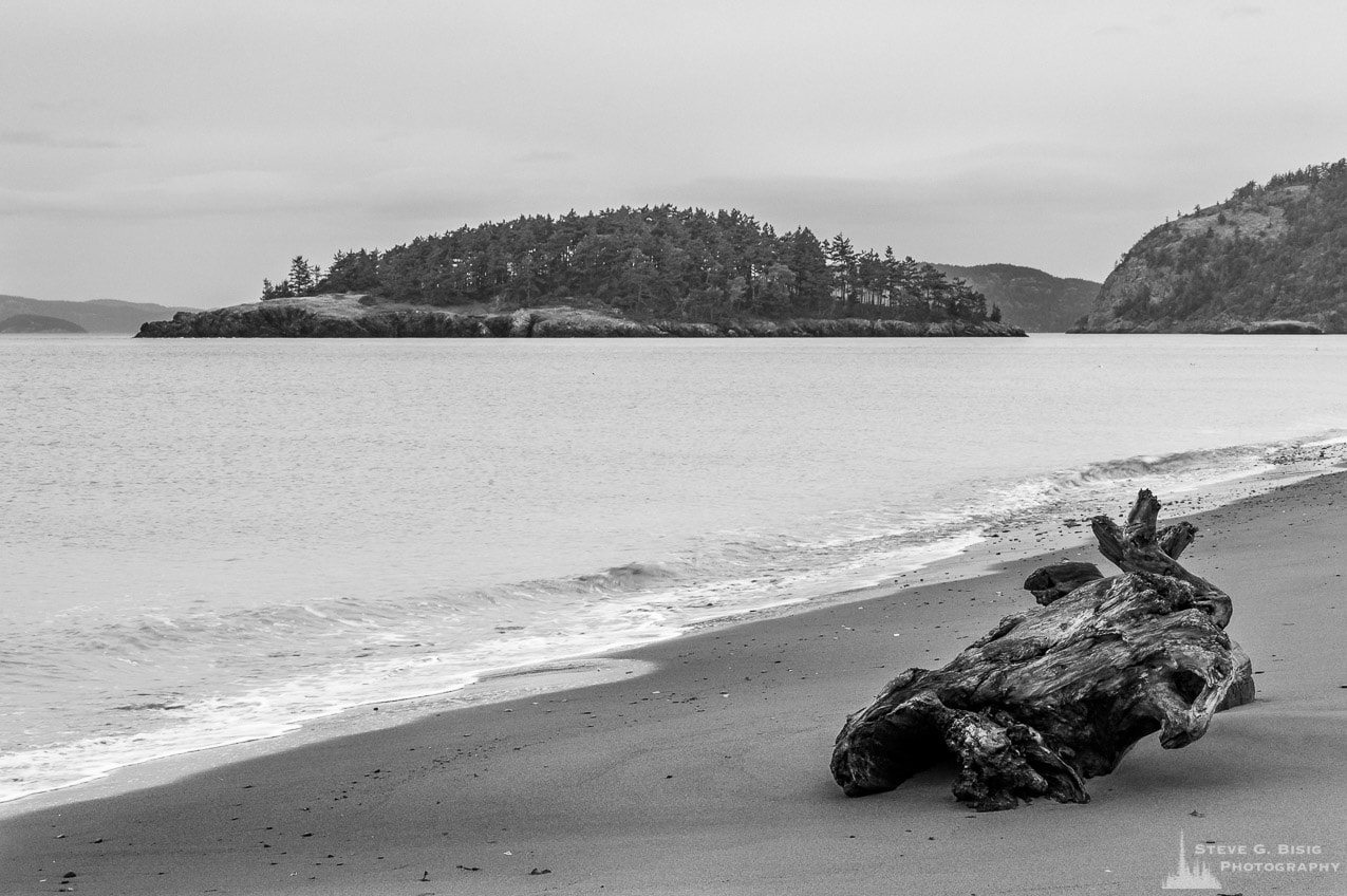 A black and white photograph of Deception Island as seen from the beach at West Point on Whidbey Island at Deception Pass State Park, Washington.