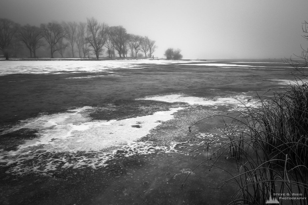 A black and white photograph of a frozen over Park Lake on a foggy Winter day at Sun Lakes State Park, Washington.