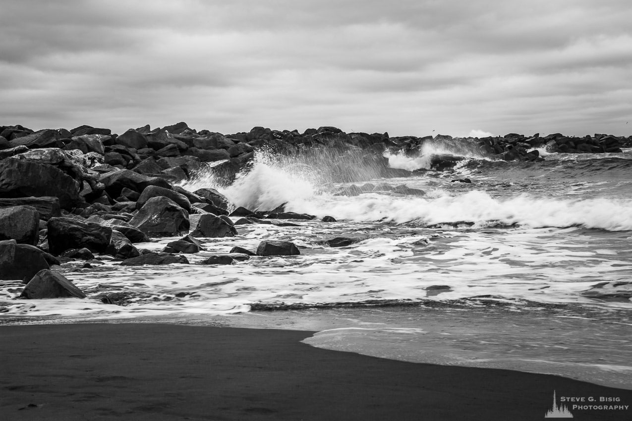 A black and white photograph of the ocean surf crashing against the North Jetty at the mouth of Grays Harbor near Ocean Shores, Washington on a cloudy Winter day.