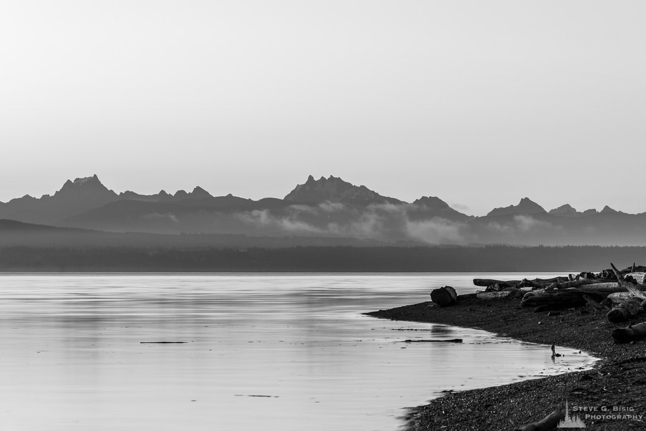 A black and white landscape photograph of Cascade Mountains in the early morning Summer light over Skagit Bay as seen from Borgman Road on Whidbey Island near Oak Harbor, Washington.