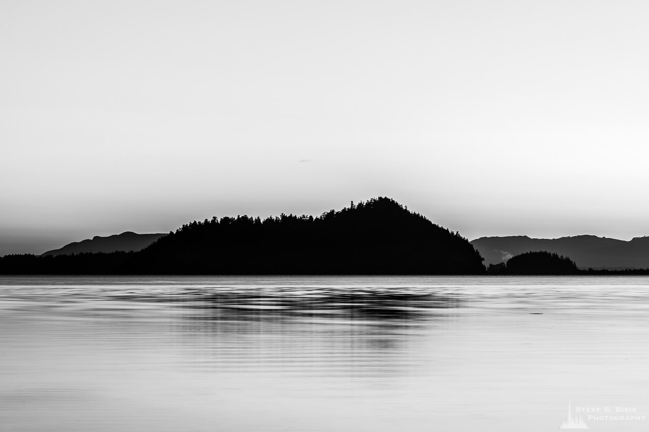 A black and white landscape photograph of Goat Island in the early morning Summer light over Skagit Bay as seen from Borgman Road on Whidbey Island near Oak Harbor, Washington.