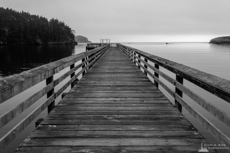A black and white landscape photograph of the Bowman Bay Dock on a foggy Summer morning at Deception Pass State Park, Washington.