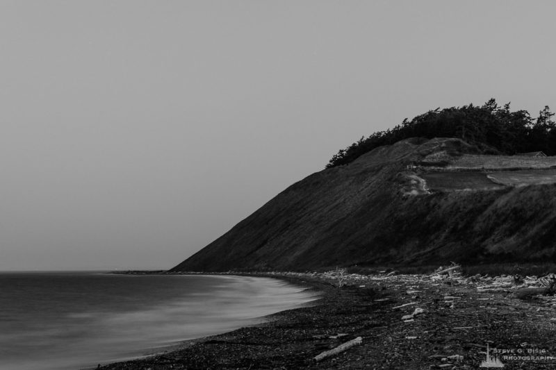 A black and white, long exposure photograph of the pre-dawn darkness along the shoreline of Ebey's Landing on Whidbey Island near Coupeville, Washington.
