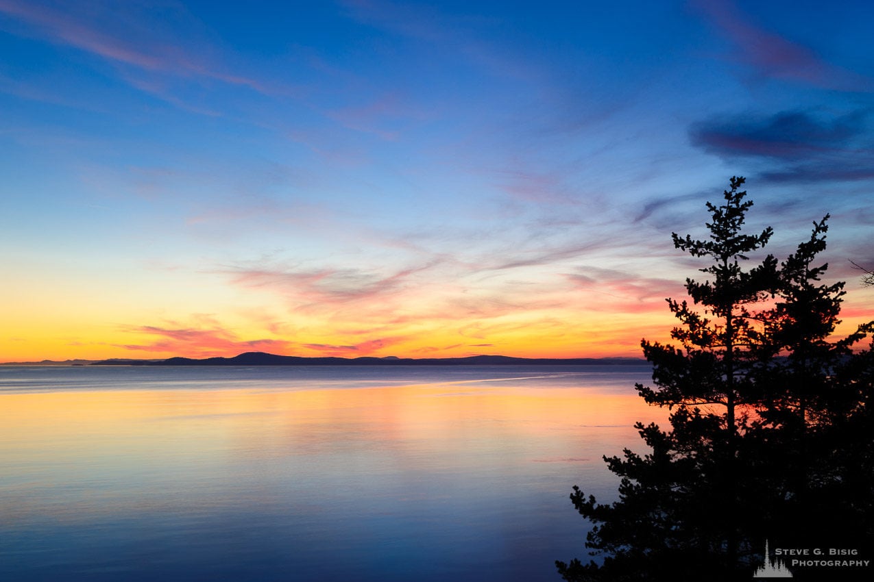 A landscape photograph of the setting sun over Northwest Pass at Deception Pass State Park, Washington.