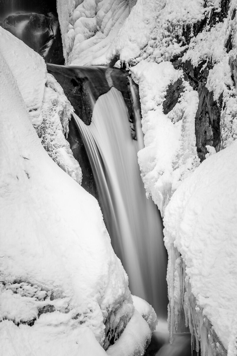 A black and white nature photograph of a snow covered, partially fozen Christine Falls at Mount Rainier National Park, Washington.