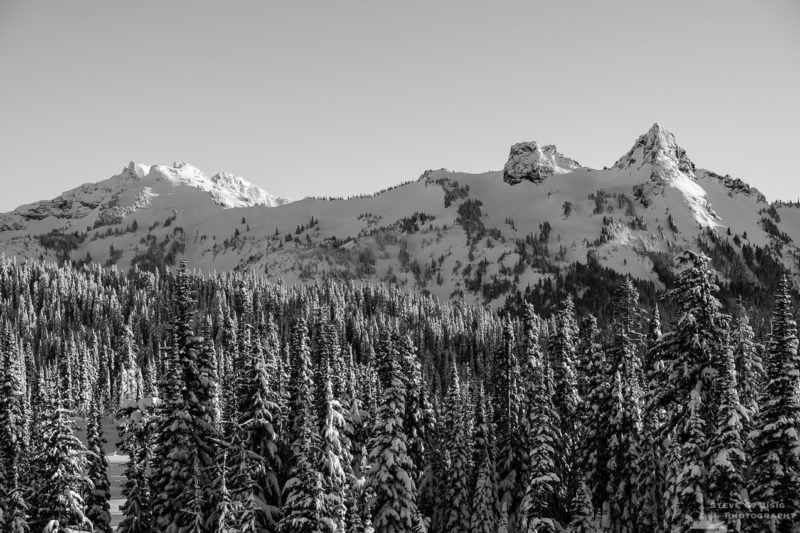 A black and white Pacific Northwest landscape photograph of a snow-covered Tatoosh Range (Pinnacle Peak, The Castle and Unicorn Peak) captured on a sunny winter day in the Paradise area of Mount Rainier National Park, Washington.