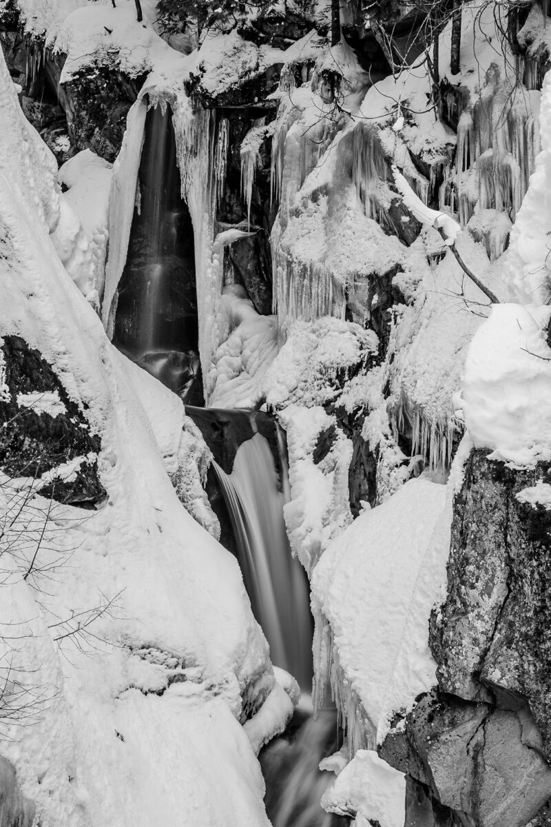A black and white nature photograph of a snow covered, partially fozen Christine Falls at Mount Rainier National Park, Washington.