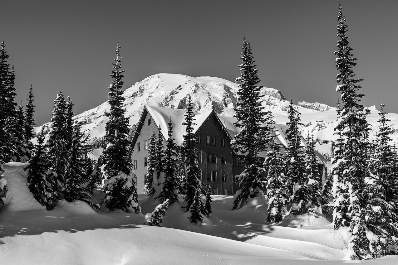 A black and white photograph of Mount Rainier and the Paradise Inn on a sunny winter day in the Paradise area of Mount Rainier National Park, Washington.