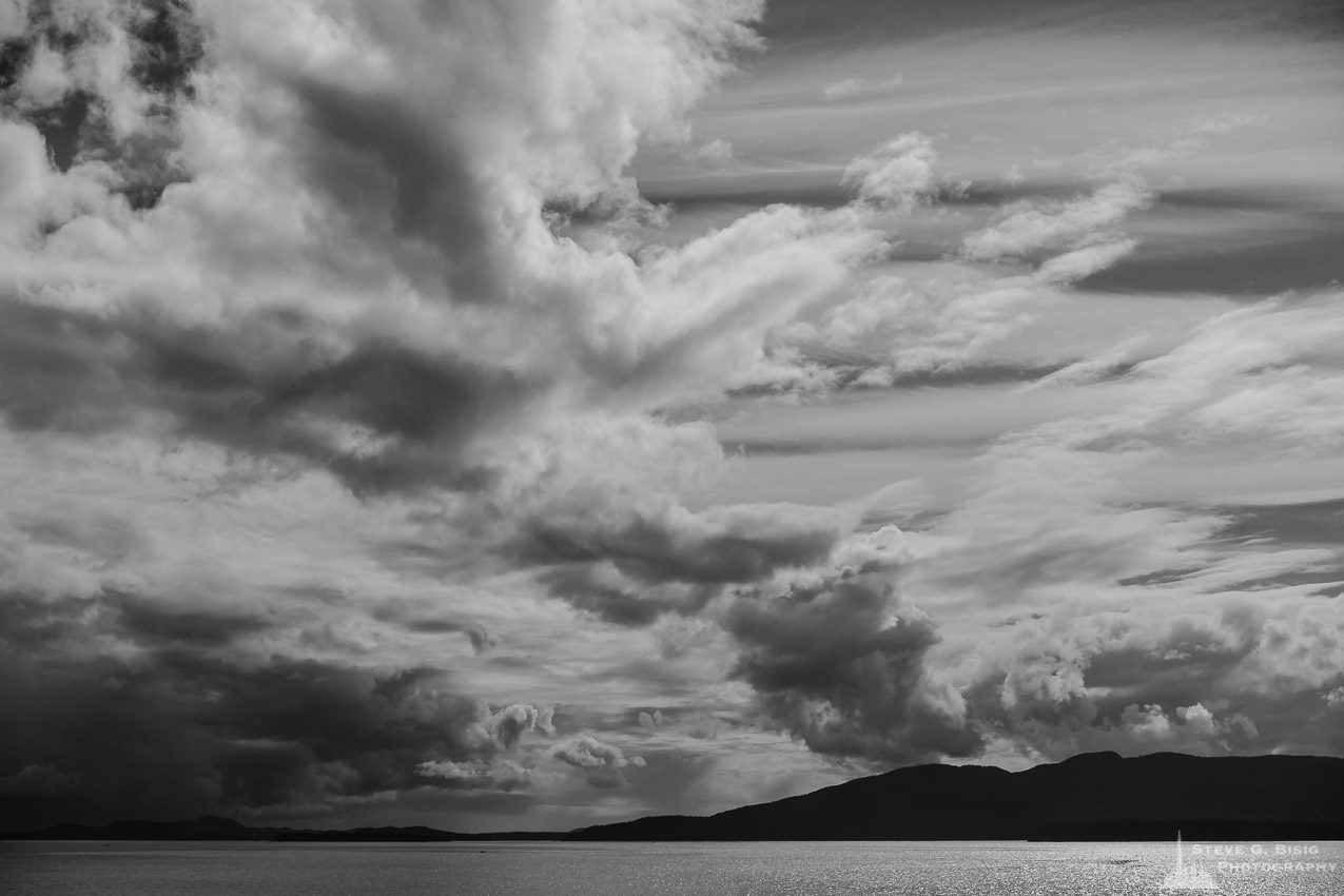 A black and white landscape photograph of storm clouds hanging over Bellingham Bay and Lummi Island as viewed from Marine Drive Park in the community of Marietta-Alderwood in Whatcom County near Bellingham, Washington.