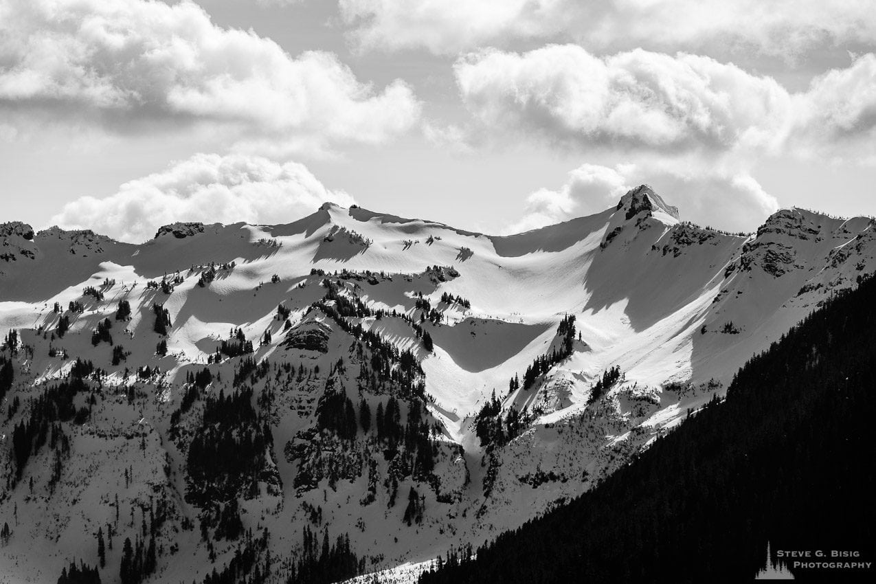 A black and white landscape photograph of the snow covered Chimney Rock and surrounding mountain ranges in the Goat Rocks Wilderness Area as viewed from Gifford Pinchot National Forest Road 1284 in Lewis County, Washington.