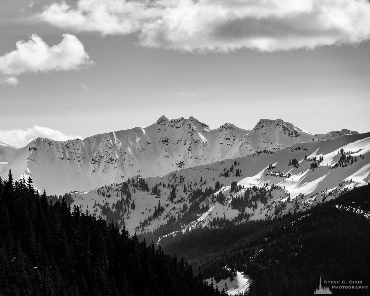 A black and white landscape photograph of the snow covered mountain ranges in the Goat Rocks Wilderness Area as viewed from Gifford Pinchot National Forest Road 1284 in Lewis County, Washington.