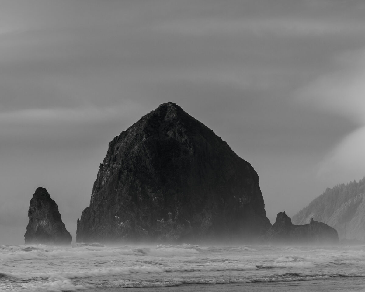 A landscape photograph of Haystack Rock and the Pacific Ocean surf along Tolovana Beach State Recreation Site at Connon Beach, Oregon.