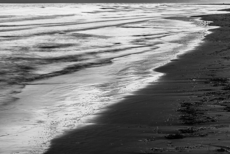 A black and white landscape photograph of the waves along the beach at North Cove, Washington.