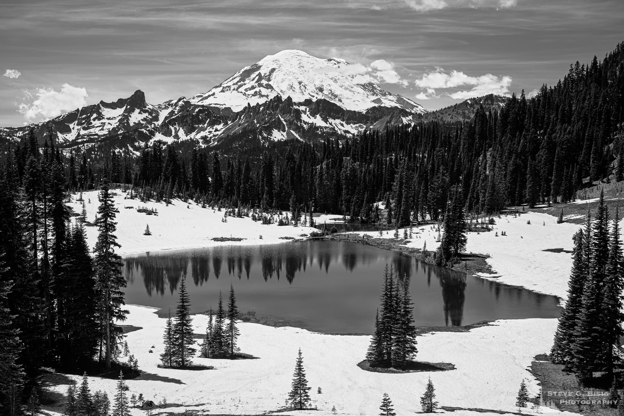 A landscape photograph of Mount Rainier as seen from a partially snow-covered Tipsoo Lake during late spring.