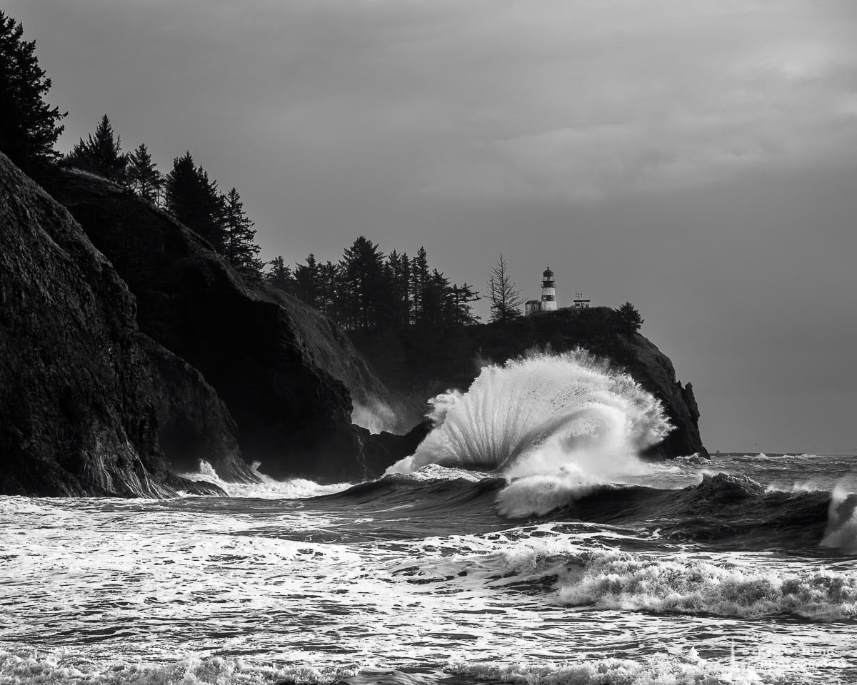 A black and white landscape photograph of the surf and lighthouse at Cape Disappointment, Washington.