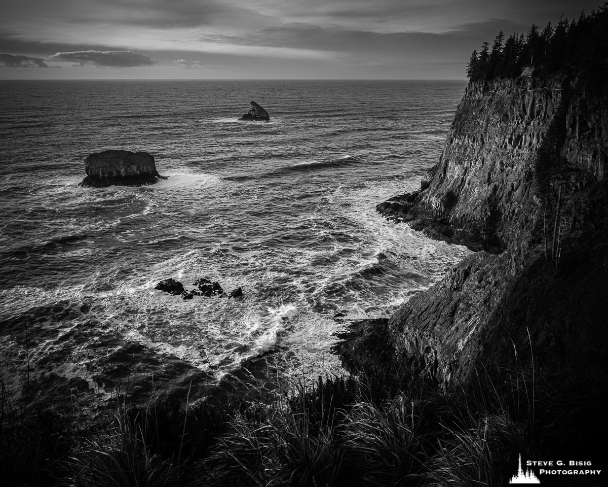 A black and white fine art landscape photograph of the bluffs along the Pacific Ocean coastline and Pillar Rock as viewed from the Cape Meares State Scenic Viewpoint near Tillamook, Oregon.