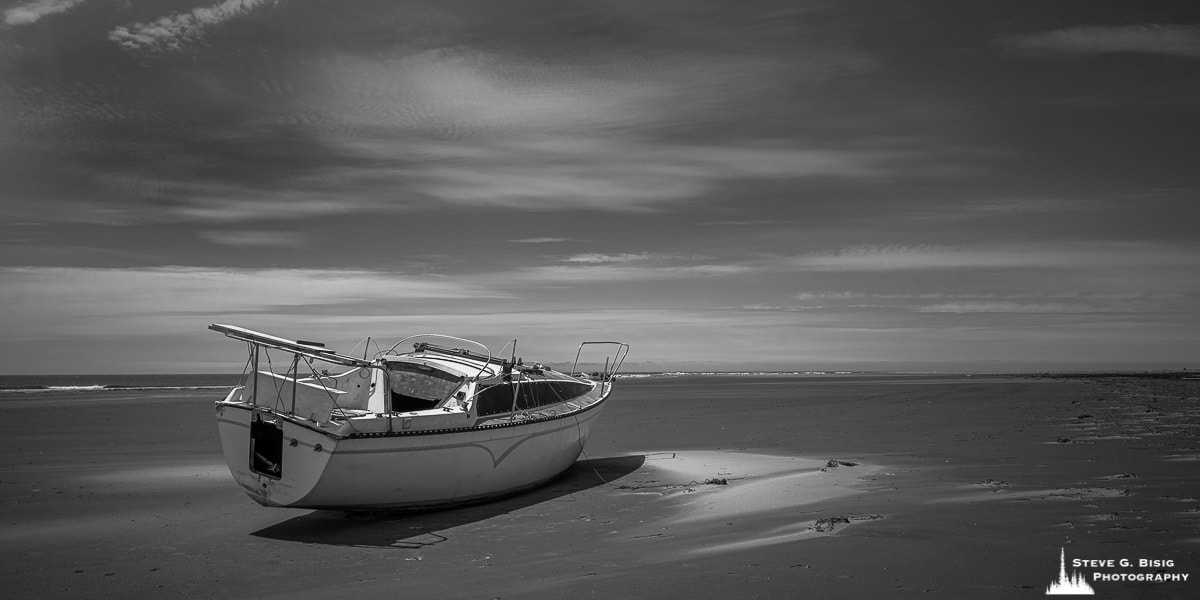A black and white photograph of a boat marooned on the beach at North Cove, Washington.