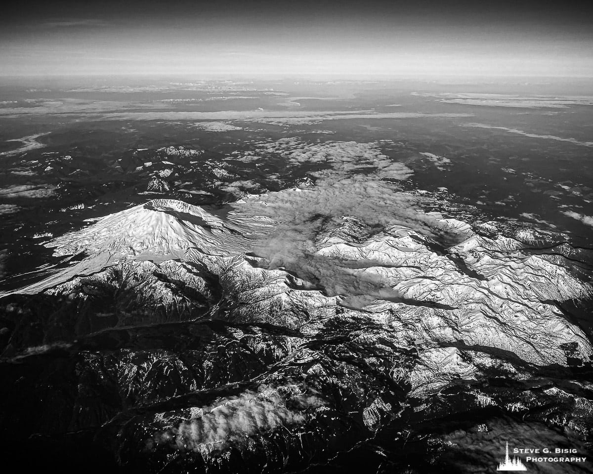 A black and white mobile aerial photograph of a snow-covered Mount Saint Helens and surrounding terrain.