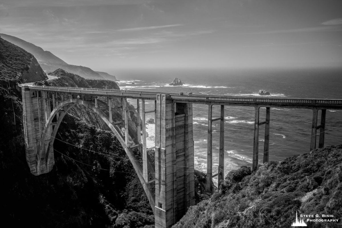 A black and white landscape photograph of the Bixby Creek Bridge and Pacific Ocean along the Cabrillo Highway 1, California.