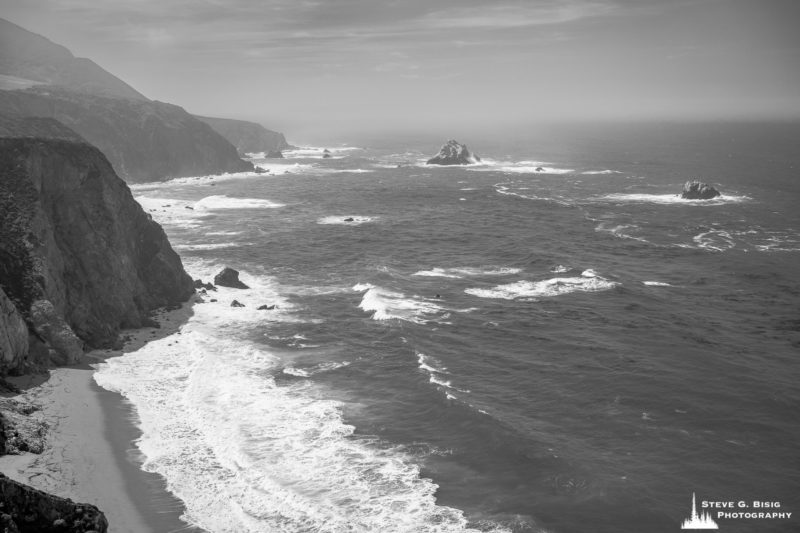 A black and white landscape photograph of the Pacific Ocean and coastline along the Cabrillo Highway 1 near Bixby Creek, California.