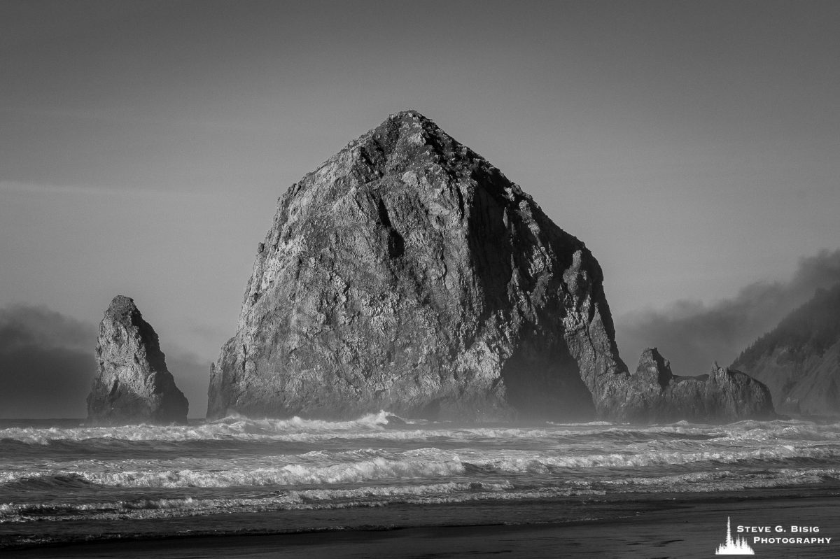 A black and white photograph of Haystack Rock captured on an early winter afternoon in Cannon Beach, Oregon.