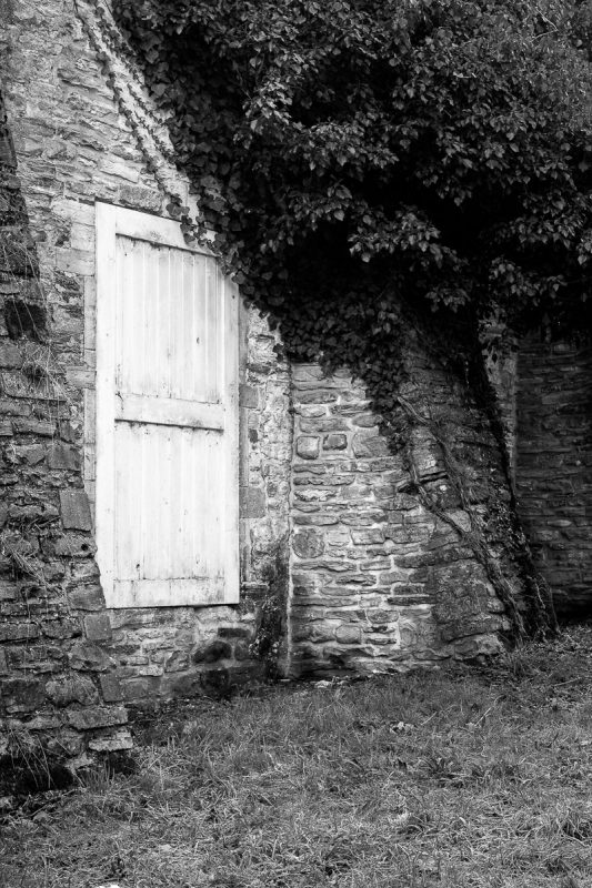 A black and white photograph of a door through a stone wall of an old agricultural building at Rouge Cloître, Auderghem, Belgium.