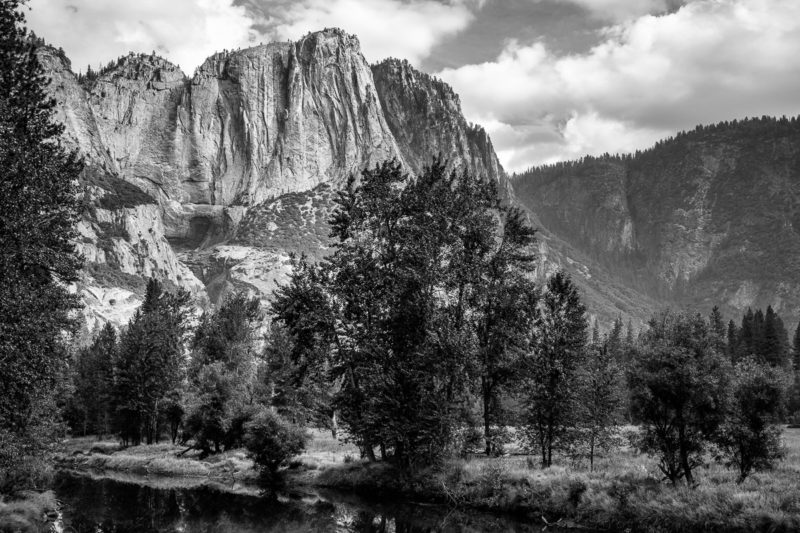 A black and white landscape photograph of the Merced River and a dry Yosemite Falls on an autumn morning in Yosemite National Park, California.