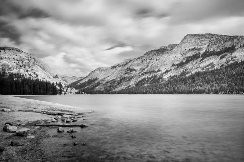 A black and white long exposure landscape photograph of Tenaya Lake and the high Sierra on an autumn day in Yosemite National Park, California.