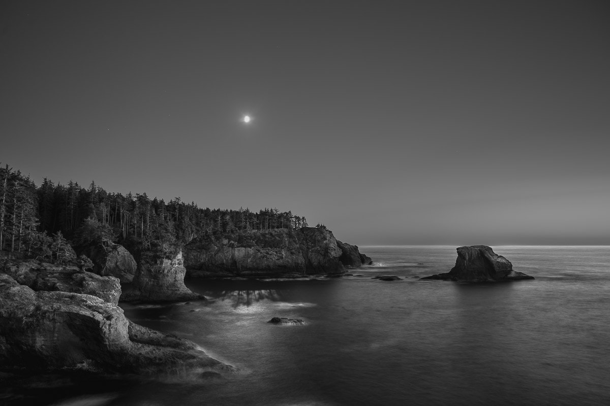 A black and white landscape photograph of the moonlight shining on the coastline over the Pacific Ocean at Cape Flattery, Washington.