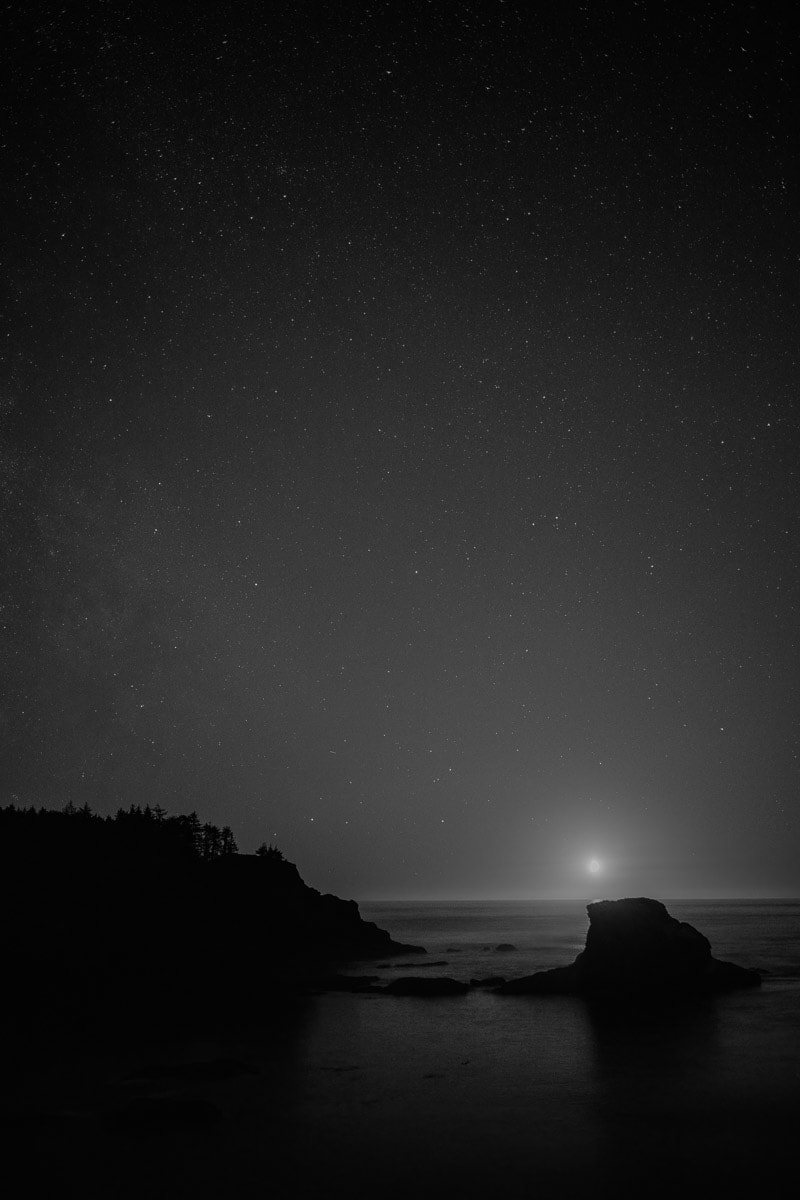 A black and white landscape photograph of the stars above the Pacific Ocean at Cape Flattery, Washington.