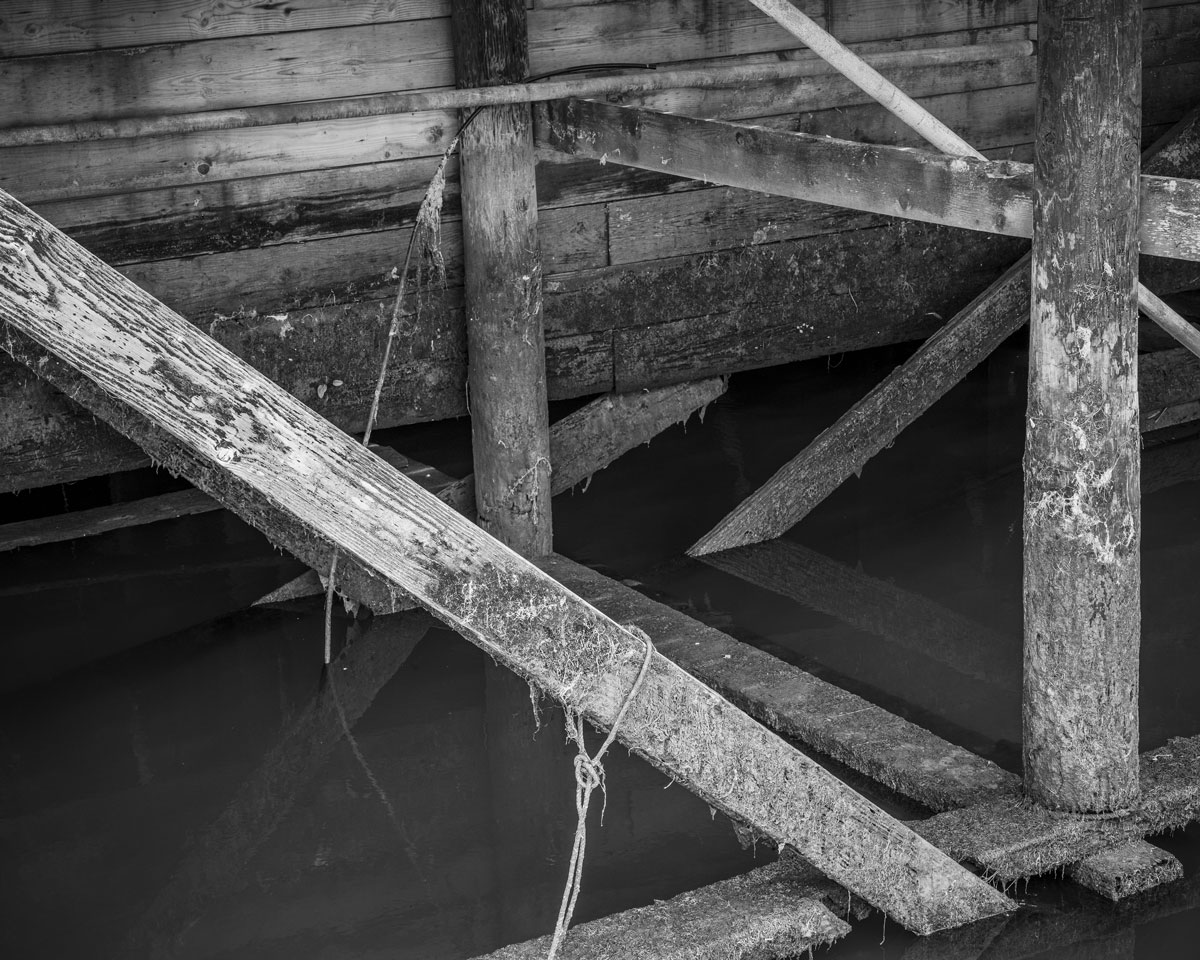 A black and white photograph of the supoorting structures under the marina in Astoria, Oregon.