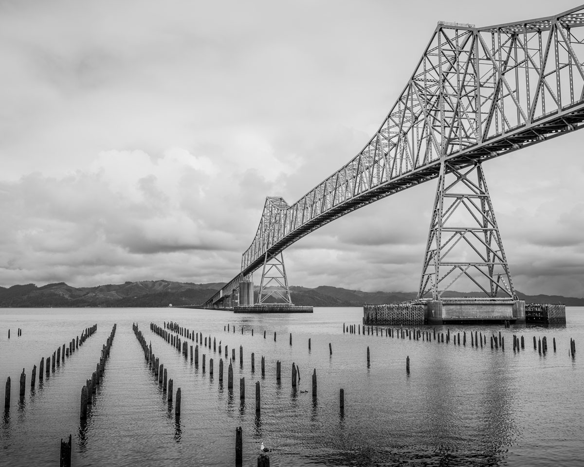 A black and white landscape photograph of the Astoria-Megler Bridge spanning the Columbia River at Astoria, Oregon.