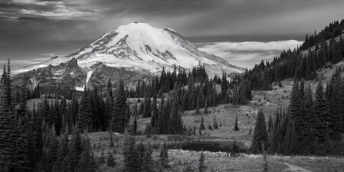A black and white panoramic landscape photograph of Mt. Rainier as viewed along the Naches Peak Loop trail near Chinook Pass, Washington.