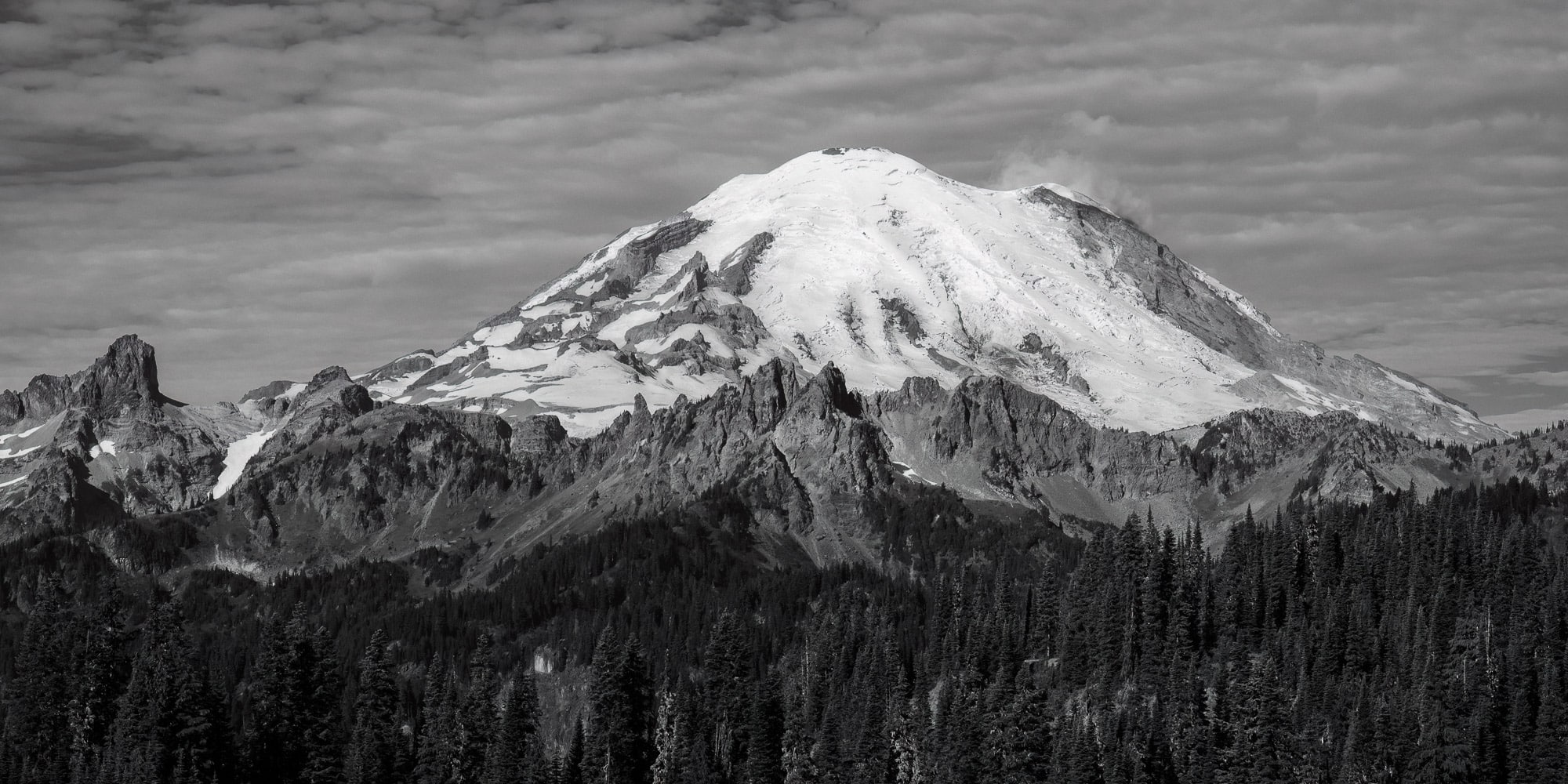 A black and white panoramic landscape photograph of Mt. Rainier and the Cowlitz Chimneys as viewed along the Naches Peak Loop trail near Chinook Pass, Washington.